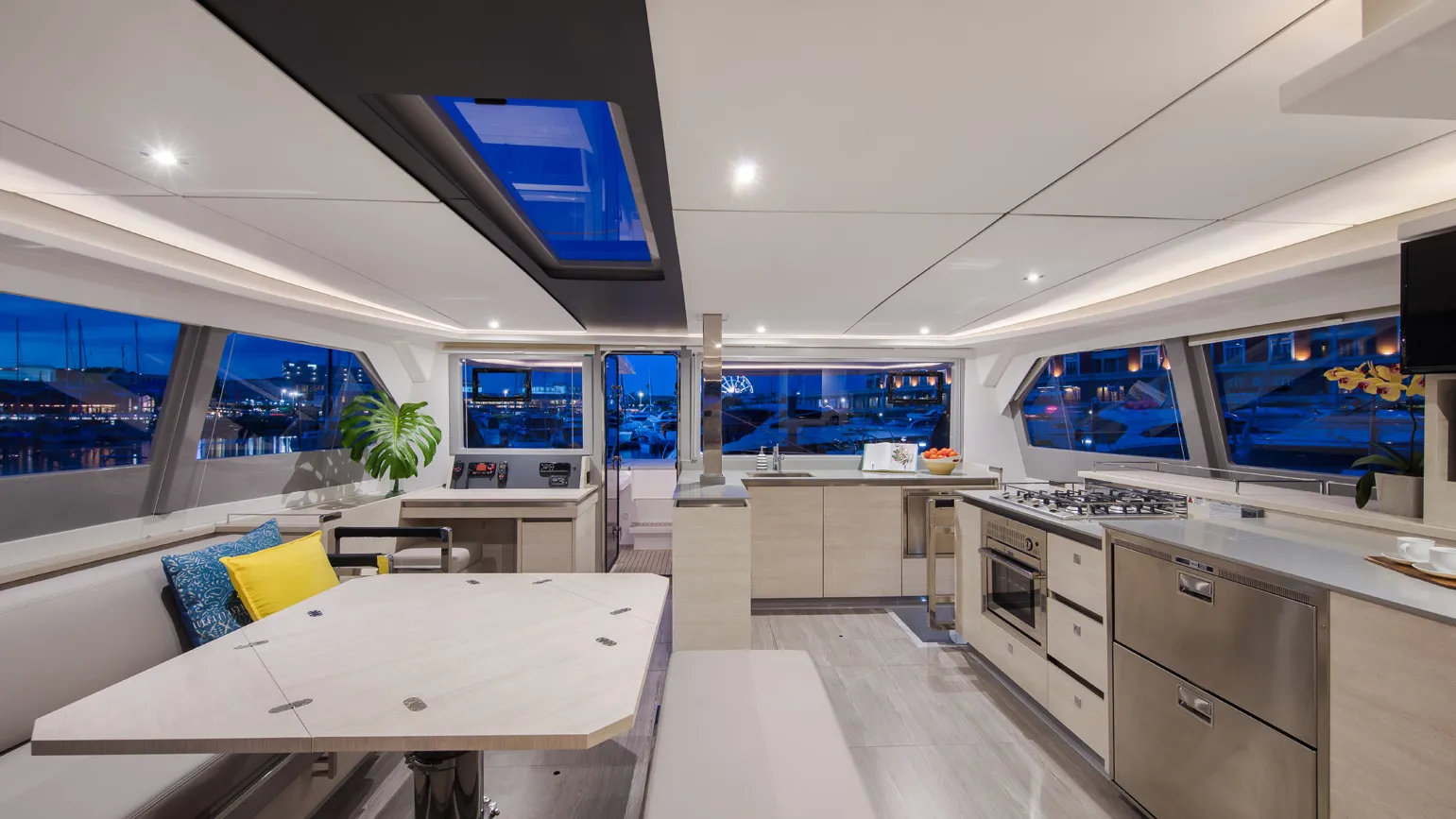 Open-plan saloon and galley at night, looking out to the marina